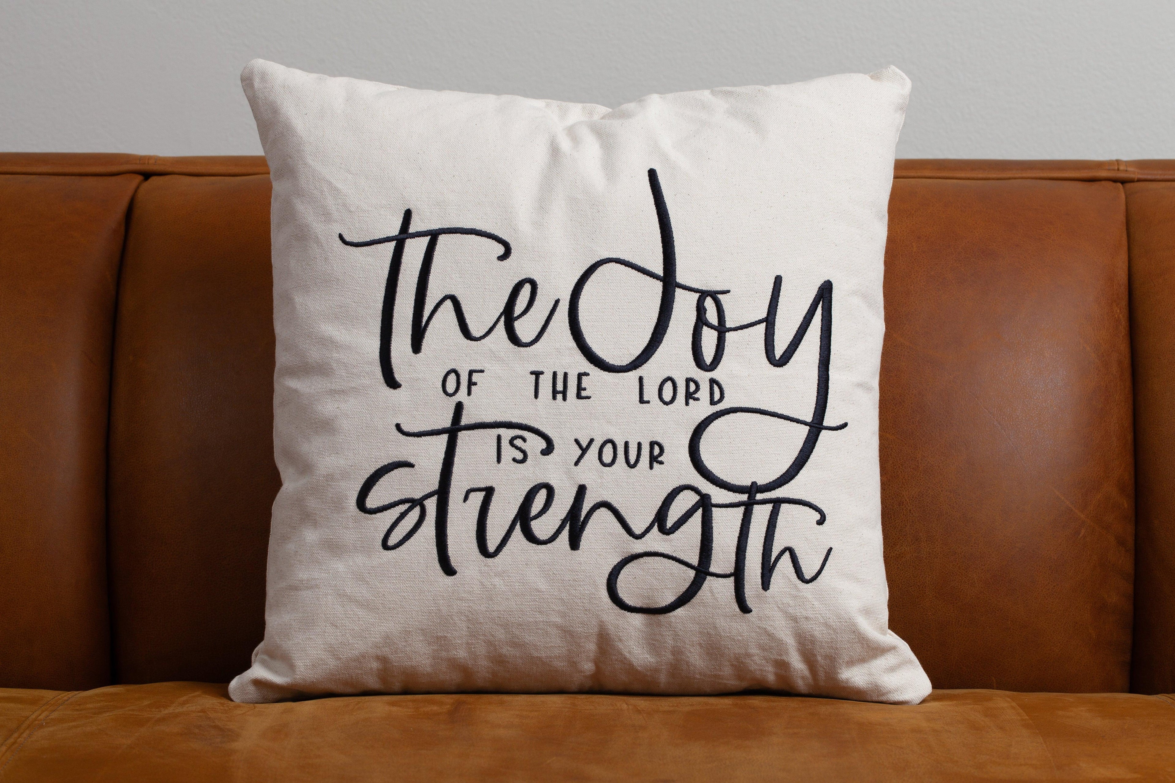 Wheat Joy & Strength throw pillow on brown leather sofa – gentle embroidered Nehemiah 8:10 complements comforting faith-filled home decor