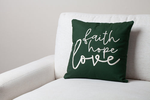 Green Faith Hope Love embroidered throw pillow on white sofa – uplifting 1 Corinthians 13:13 verse brings hope to contemporary faith decor