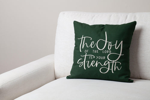 Green Joy & Strength embroidered throw pillow on white sofa – vibrant Nehemiah 8:10 verse uplifts contemporary faith-inspired space