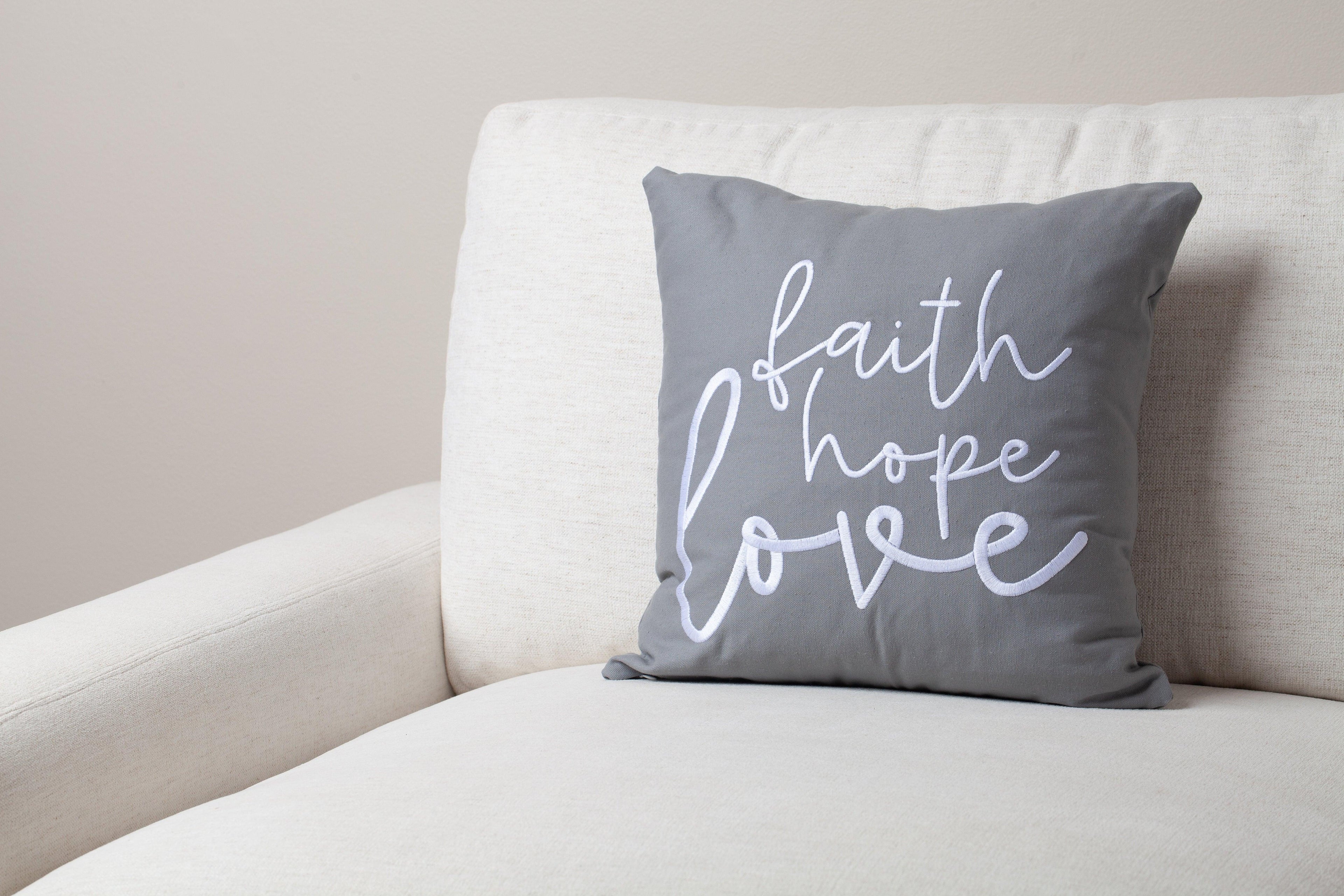 Gray Faith Hope Love Bible verse throw pillow on white couch – hand-embroidered 1 Corinthians 13:13 enhances serene inspirational home decor