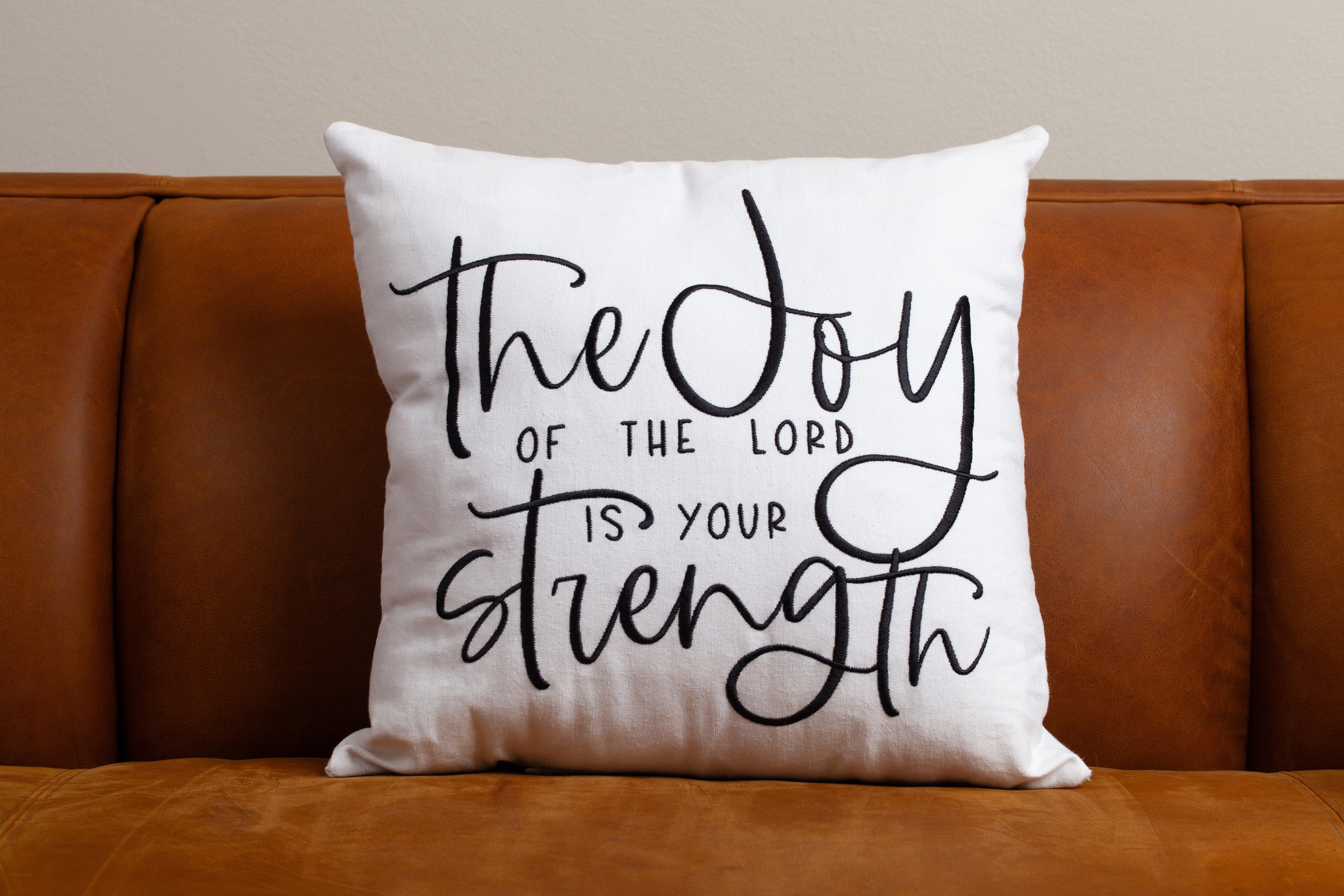 White Joy & Strength scripture pillow on brown sofa – minimalist Nehemiah 8:10 accent for peaceful empowering Christian interior